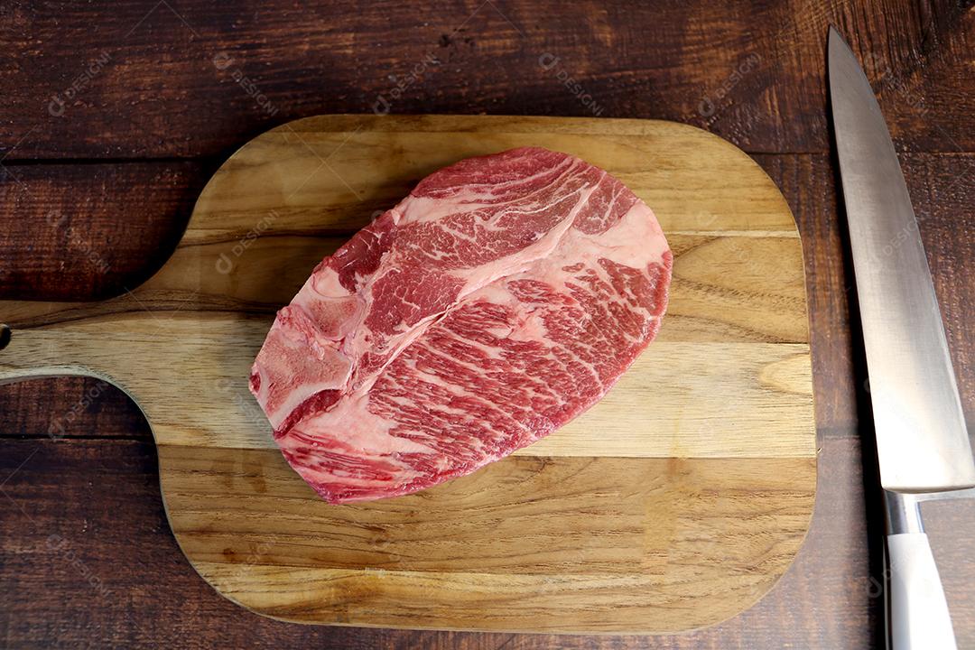 Costela Curta ou Costela Premium. Belo bife cru sob uma tábua de madeira em um fundo de madeira. Para um churrasco brasileiro JPG