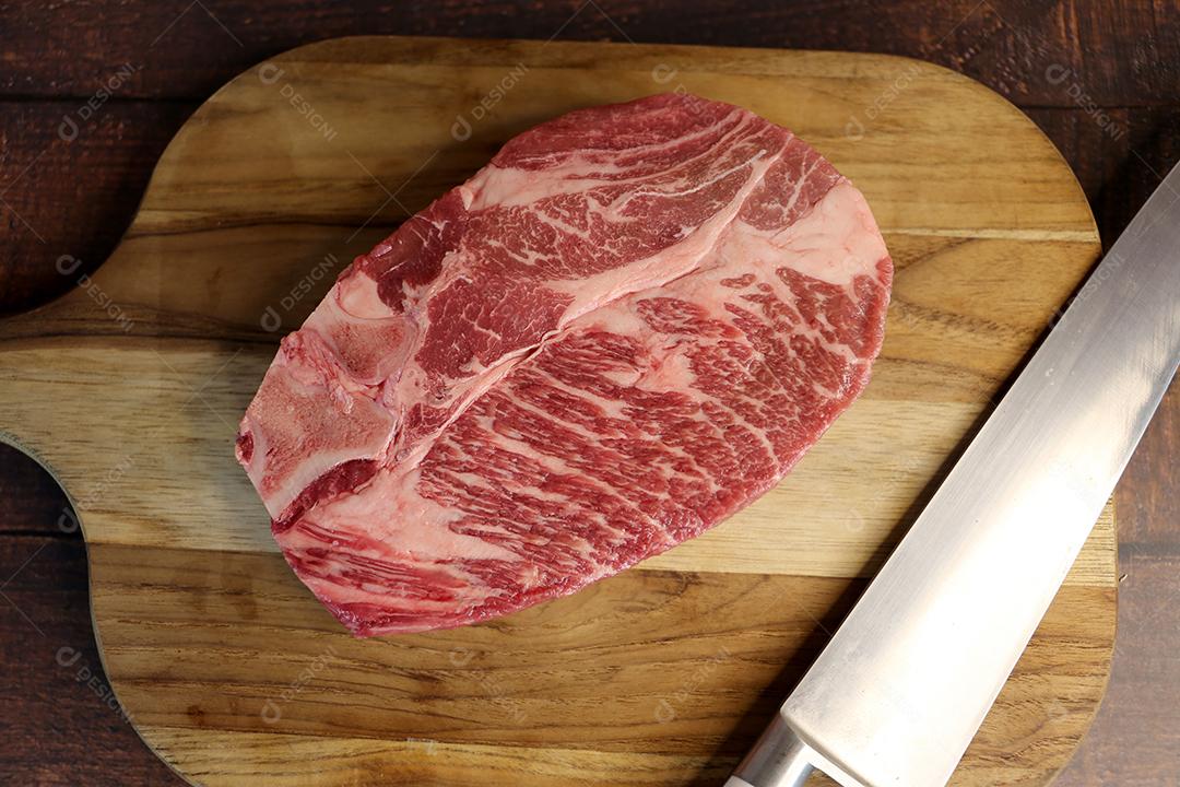 Costela Curta ou Costela Premium. Belo bife cru sob uma tábua de madeira em um fundo de madeira. Para um churrasco brasileiro JPG