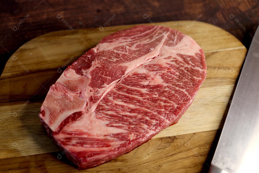 Costela Curta ou Costela Premium. Belo bife cru sob uma tábua de madeira em um fundo de madeira. Para um churrasco brasileiro JPG