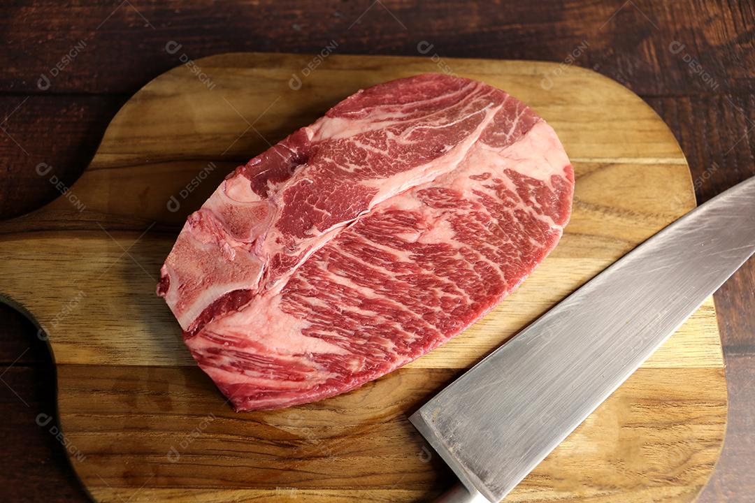 Costela Curta ou Costela Premium. Belo bife cru sob uma tábua de madeira em um fundo de madeira. Para um churrasco brasileiro JPG