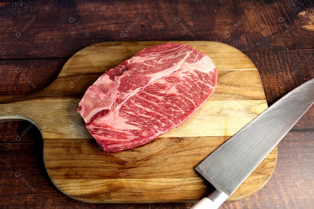 Costela Curta ou Costela Premium. Belo bife cru sob uma tábua de madeira em um fundo de madeira. Para um churrasco brasileiro JPG