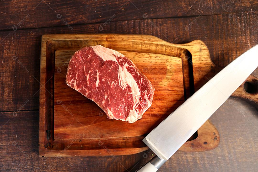 Costela Curta ou Costela Premium. Belo bife cru sob uma tábua de madeira em um fundo de madeira. Para um churrasco brasileiro JPG