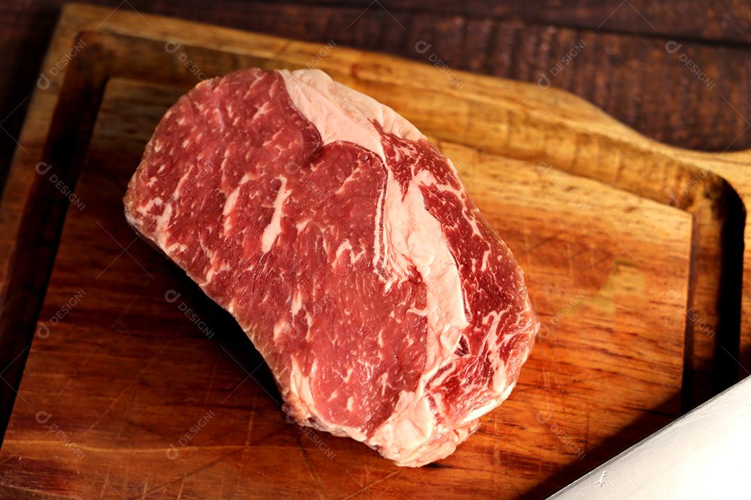 Costela Curta ou Costela Premium. Belo bife cru sob uma tábua de madeira em um fundo de madeira. Para um churrasco brasileiro JPG