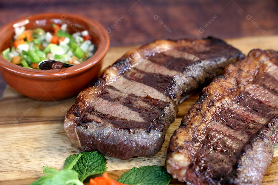 Picanha, picanha. Bife brasileiro grelhado em churrasco. Duas fatias de Picanha com molho verde, farofa, faca, vinagrete. Comida brasileira JPG