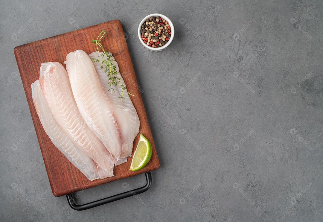 Filé de peixe de tilápia crua com temperos sobre tábua de madeira JPG