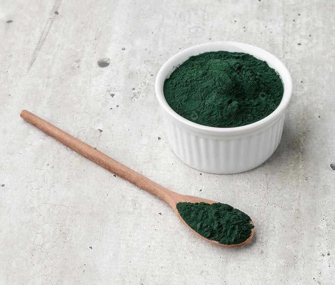 Pó de algas spirulina em uma tigela e colher sobre mesa de madeira JPG