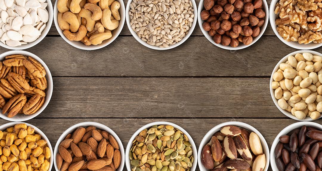 Nozes e sementes variadas em tigelas sobre mesa de madeira
