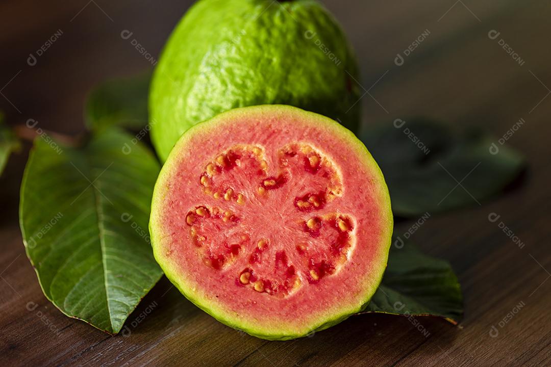 Faca de aço antiga e goiabas vermelhas fatiadas em fundo de madeira rústico Imagem JPG