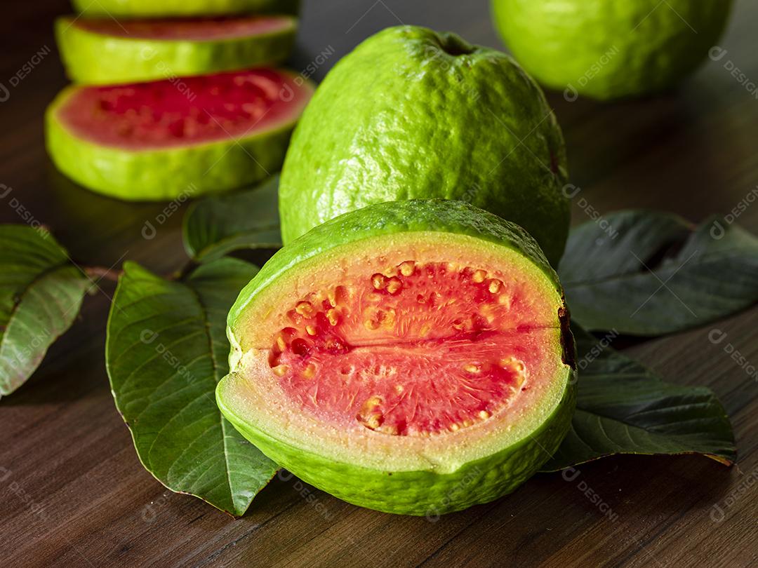 Faca de aço antiga e goiabas vermelhas fatiadas em fundo de madeira rústico Imagem JPG