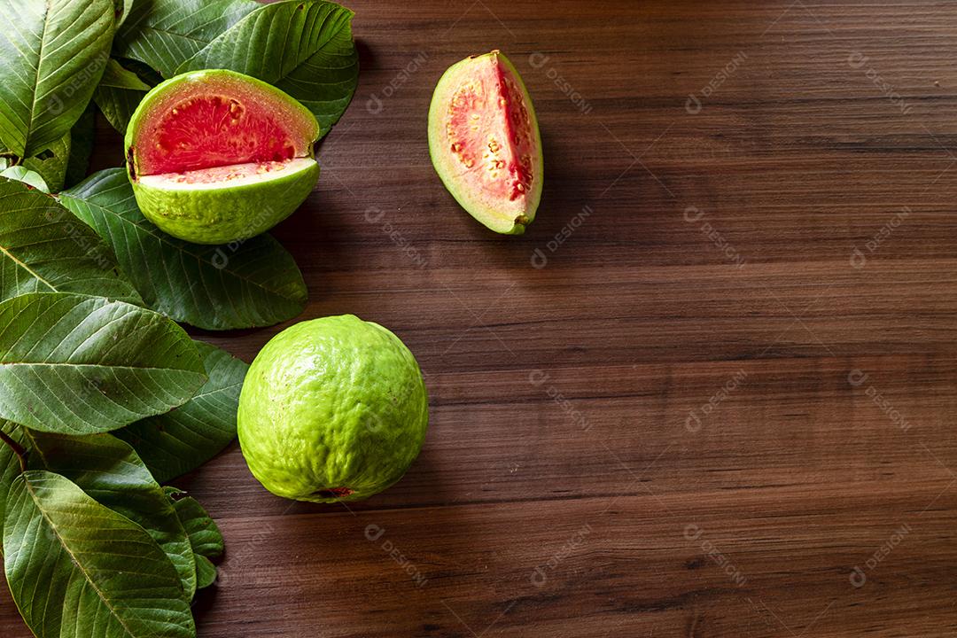 Faca de aço antiga e goiabas vermelhas fatiadas em fundo de madeira rústico Imagem JPG