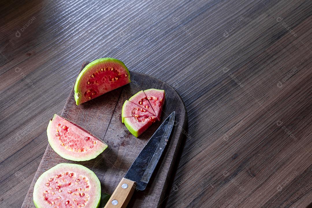 Faca de aço antiga e goiabas vermelhas fatiadas em fundo de madeira rústico Imagem JPG