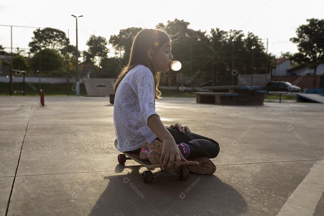 Garota sentada em um skate em uma quadra Imagem JPG