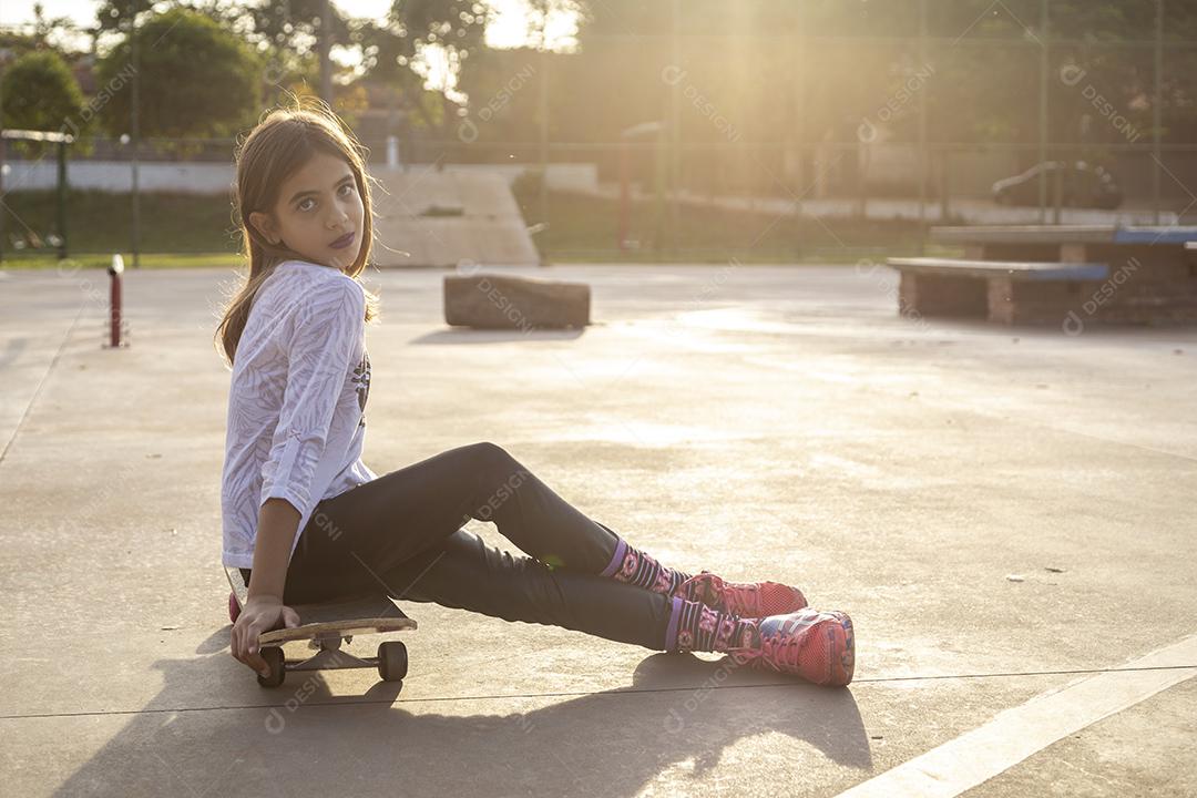 Garota sentada em um skate em uma quadra Imagem JPG