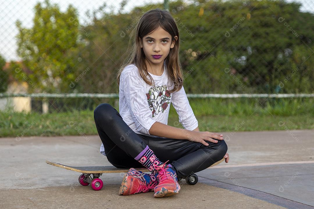 Garota sentada em um skate em uma quadra Imagem JPG