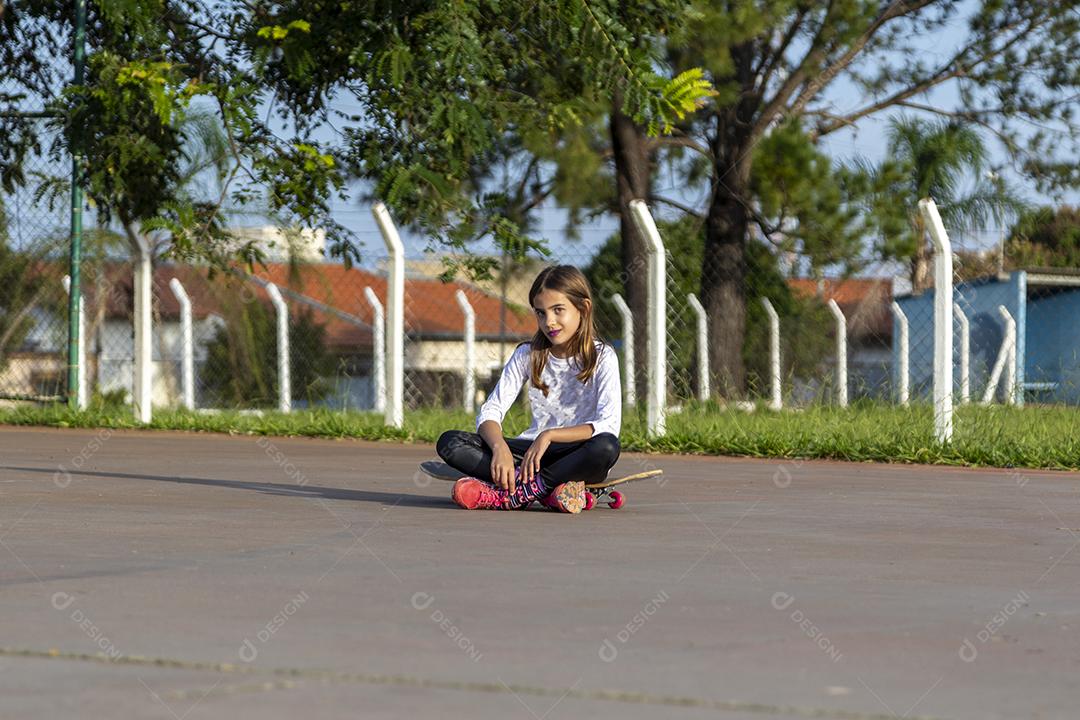 Linda loira sentada em cima do skate no parque ao pôr do sol Imagem JPG