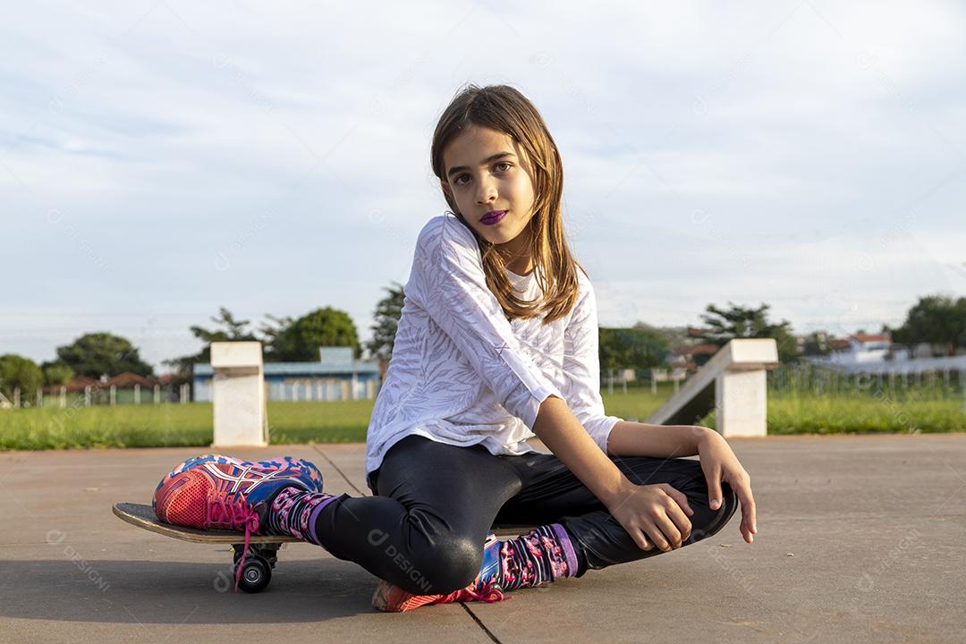 Linda loira sentada em cima do skate no parque ao pôr do sol Imagem JPG