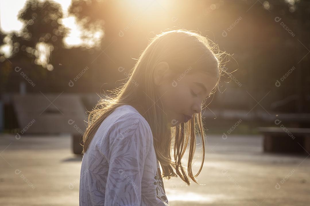 Linda loira sentada em cima do skate no parque ao pôr do sol Imagem JPG