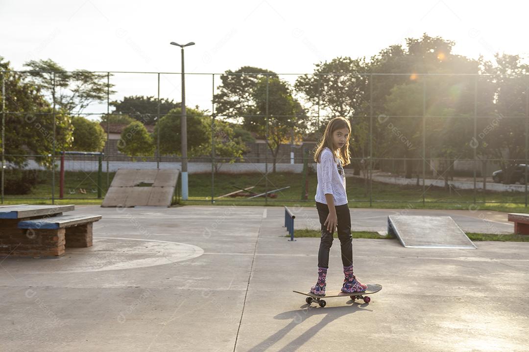 Linda loira sentada em cima do skate no parque ao pôr do sol Imagem JPG