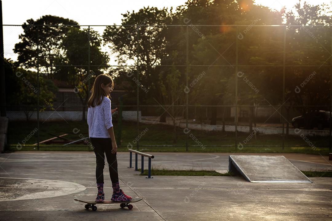 Linda loira andando de skate no parque ao pôr do sol Imagem JPG