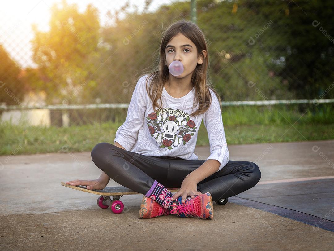 Linda loira sentada em cima do skate no parque ao pôr do sol Imagem JPG