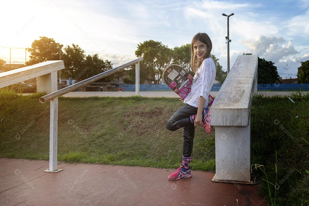 Linda loira andando de skate no parque ao pôr do sol Imagem JPG