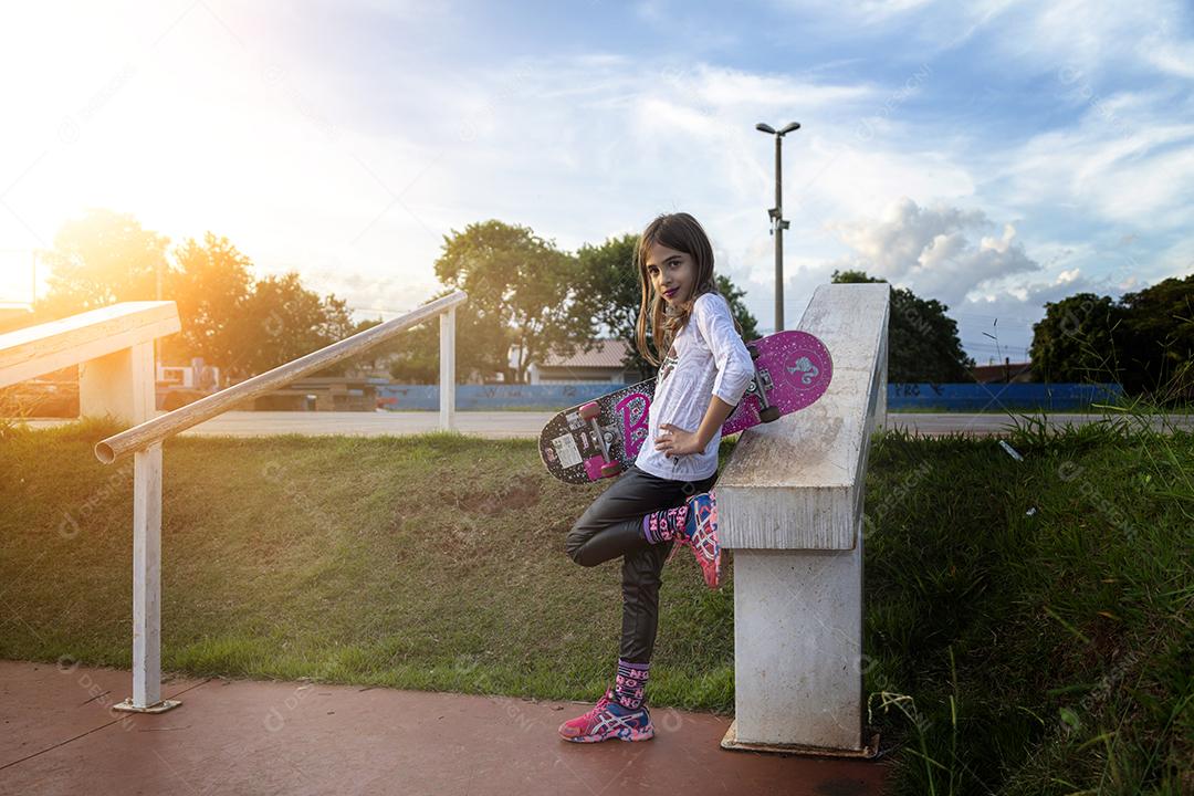 Linda loira andando de skate no parque ao pôr do sol Imagem JPG