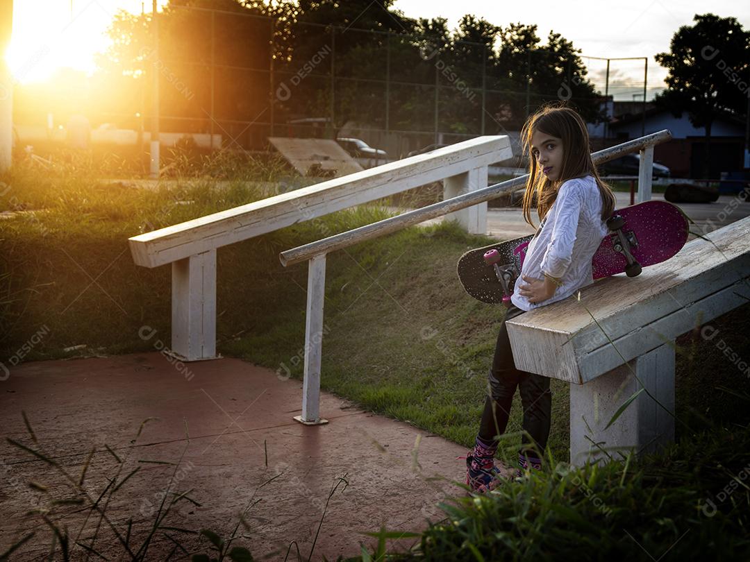 Linda loira segurando skate no parque ao pôr do sol Imagem JPG