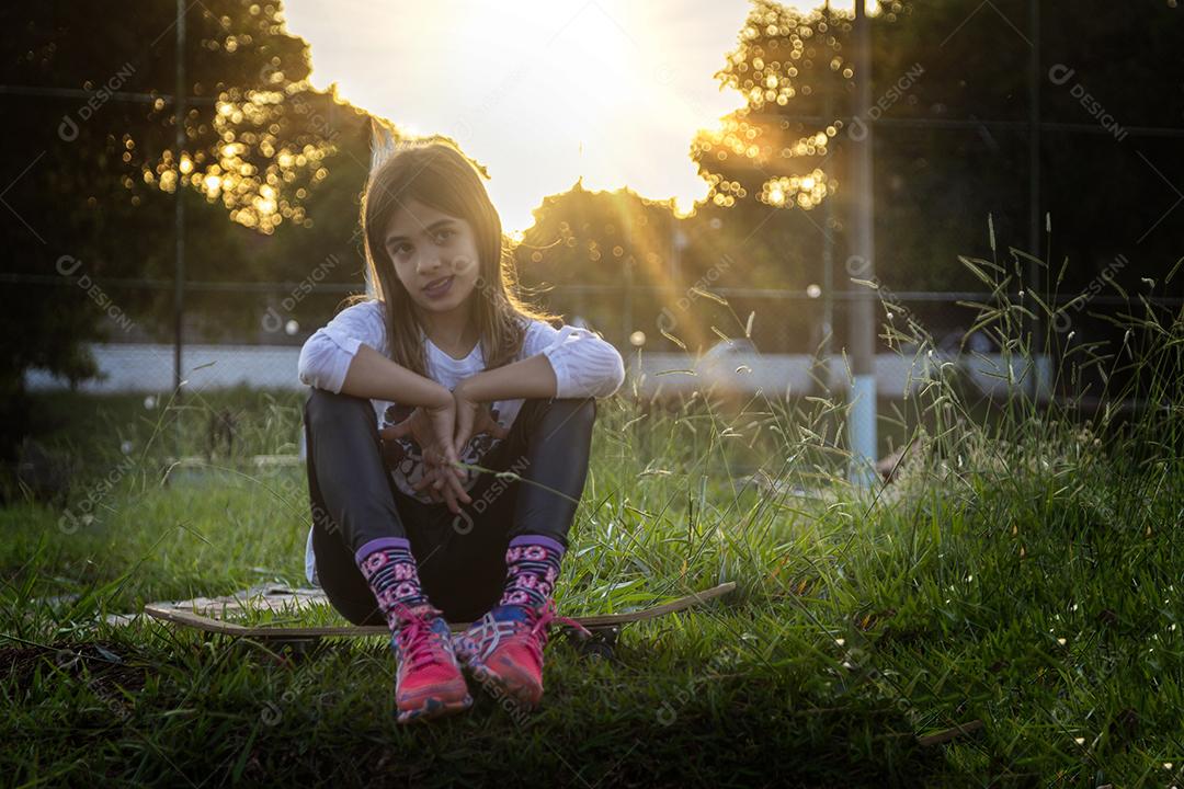 Linda loira sentada em cima do skate no parque ao pôr do sol Imagem JPG