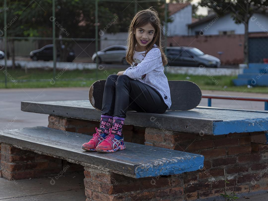 Linda loira segurando skate no parque ao pôr do sol Imagem JPG