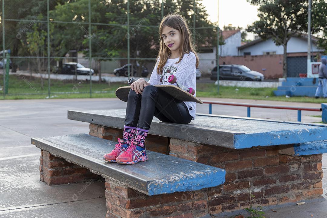 Linda loira segurando skate no parque ao pôr do sol Imagem JPG