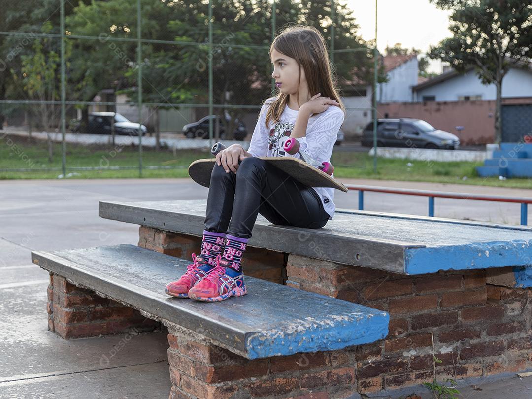 Linda loira segurando skate no parque ao pôr do sol Imagem JPG