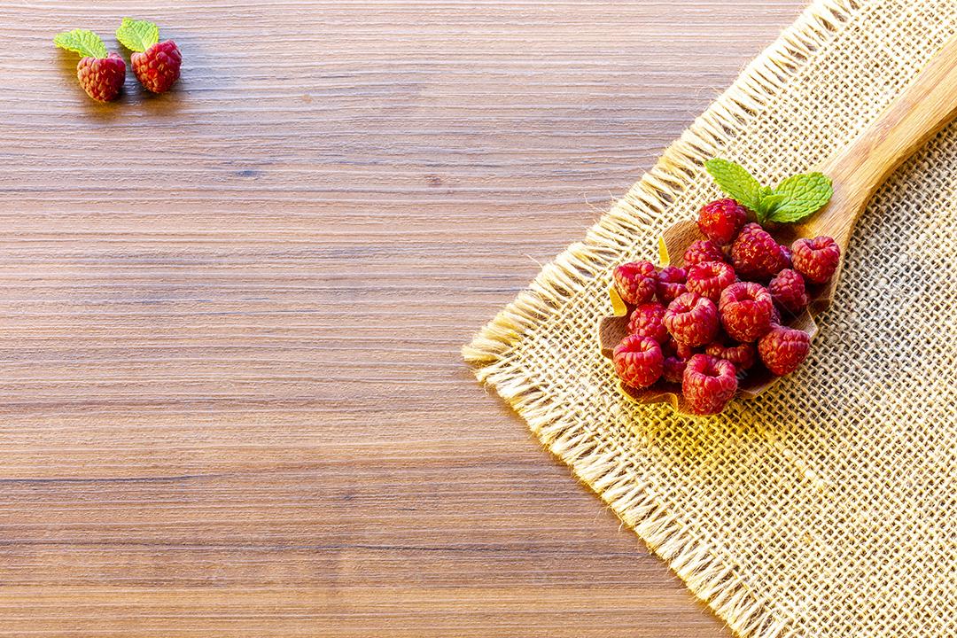 Colher com framboesa e tigela com geléia de framboesa no fundo de madeira