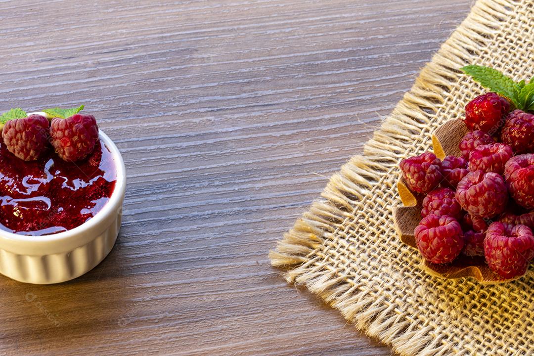 Colher com framboesa e tigela com geléia de framboesa no fundo de madeira