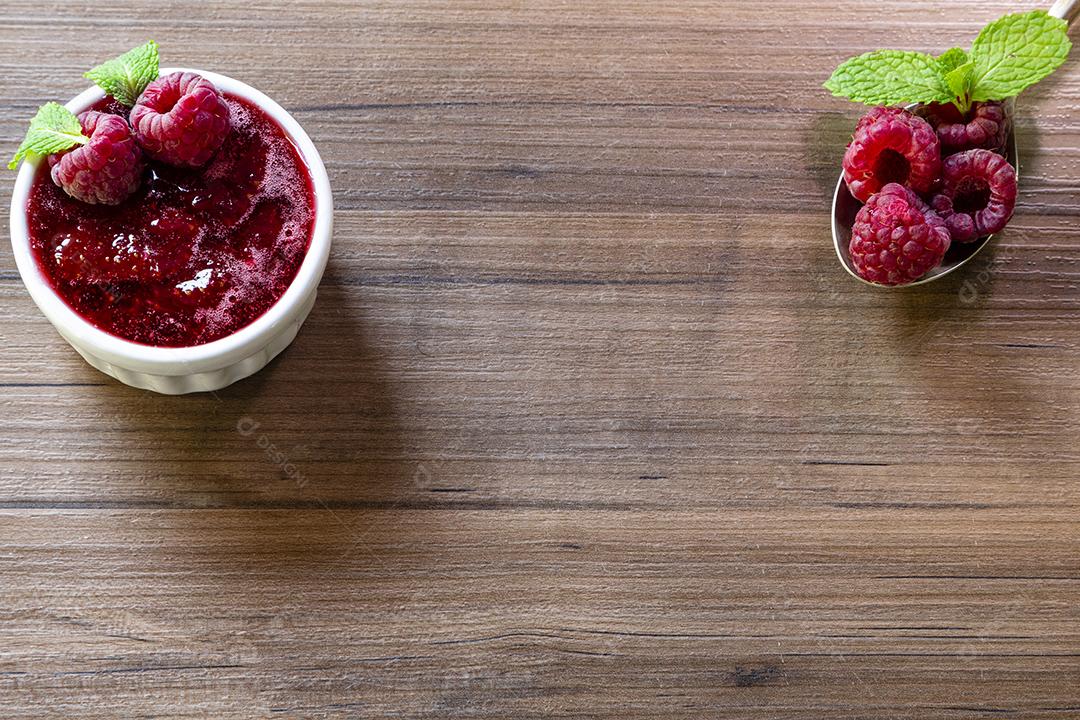 Colher com framboesa e tigela com geléia de framboesa em fundo de madeira Imagem JPG