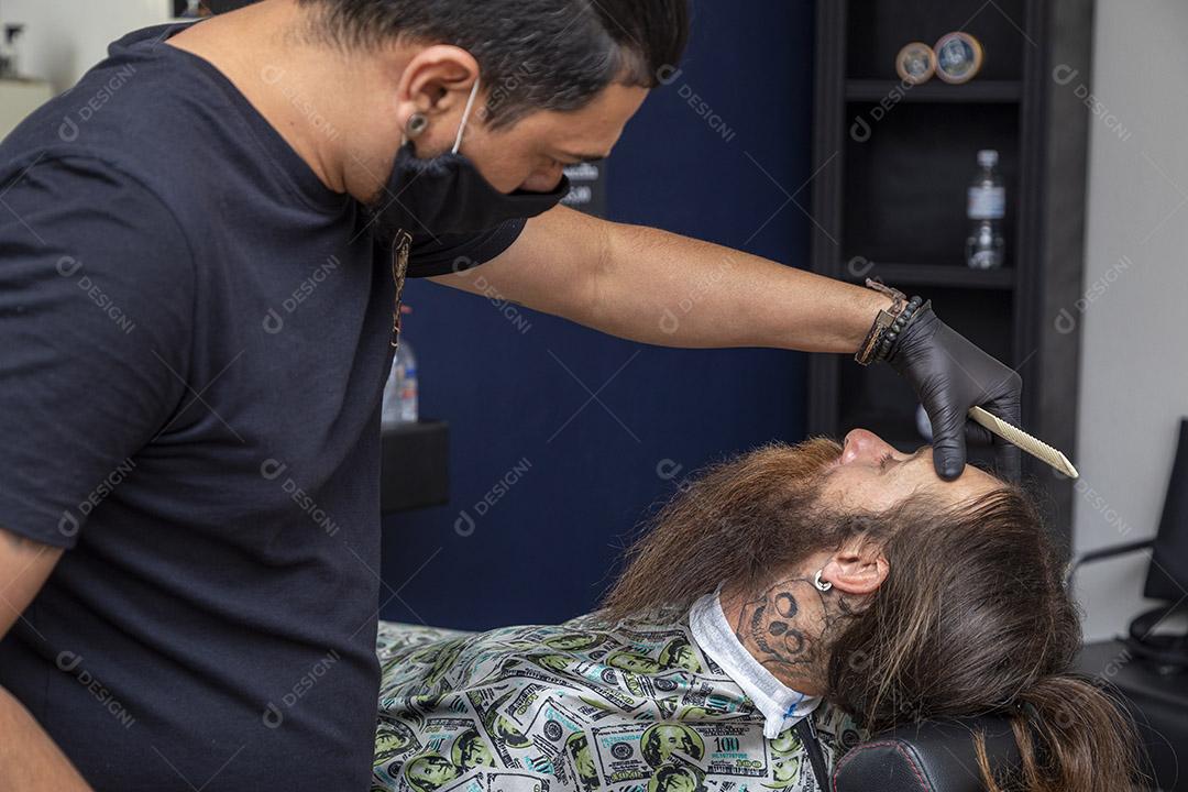 Barbeiro usando barbeador para cortar a barba de um homem. Imagem JPG