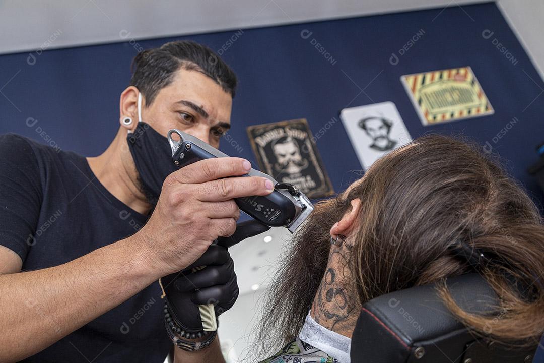 Barbeiro usando barbeador para cortar a barba de um homem. Imagem JPG