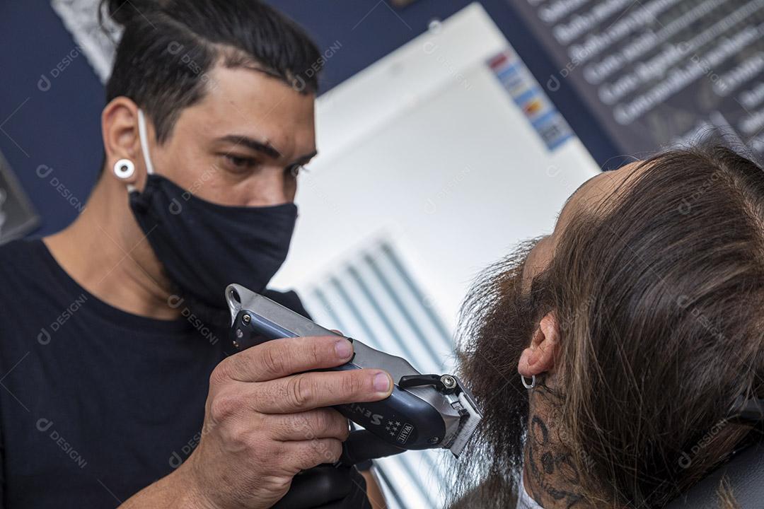 Barbeiro usando barbeador para cortar a barba de um homem. Imagem JPG