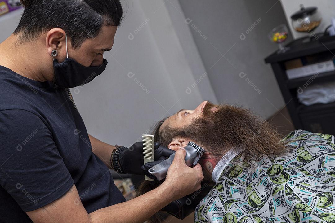Barbeiro usando barbeador para cortar a barba de um homem. Imagem JPG
