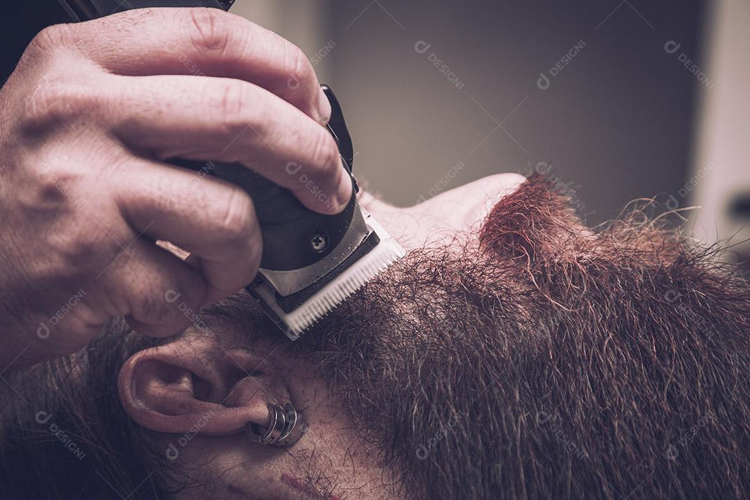 Barbeiro usando barbeador para cortar a barba de um homem. Imagem JPG