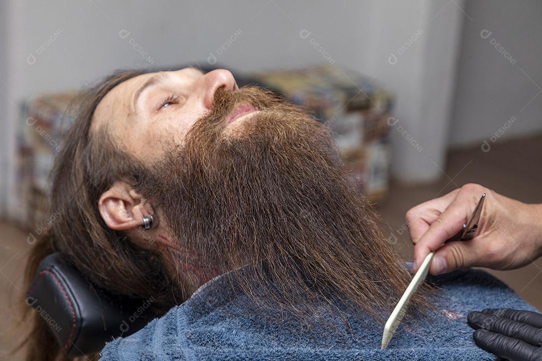 Barbeiro penteando a barba vermelha na barbearia.Imagem JPG