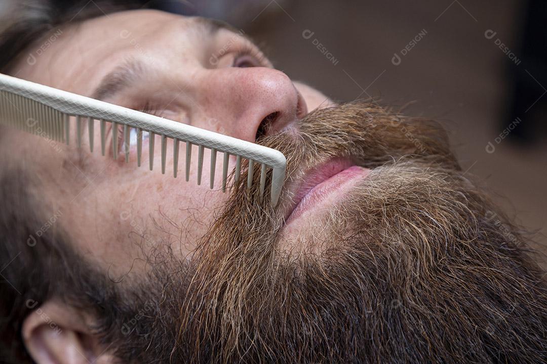 Barbeiro penteando a barba ruiva na barbearia Imagem JPG