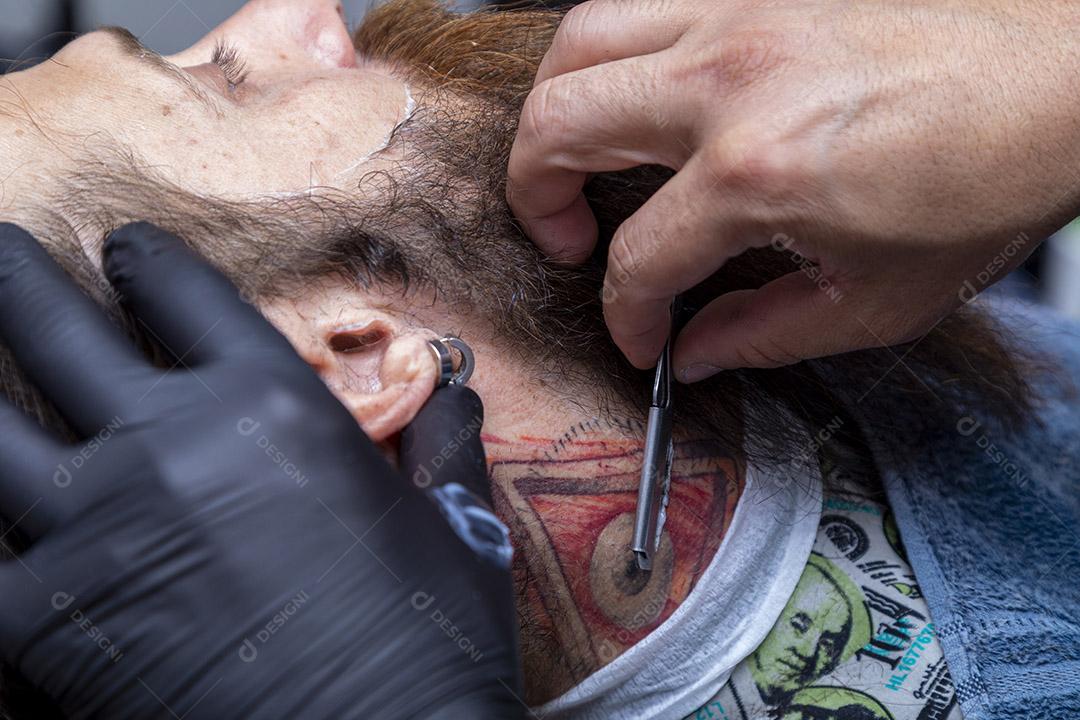 Barbeiro usando barbeador para cortar a barba de um homem. Imagem JPG