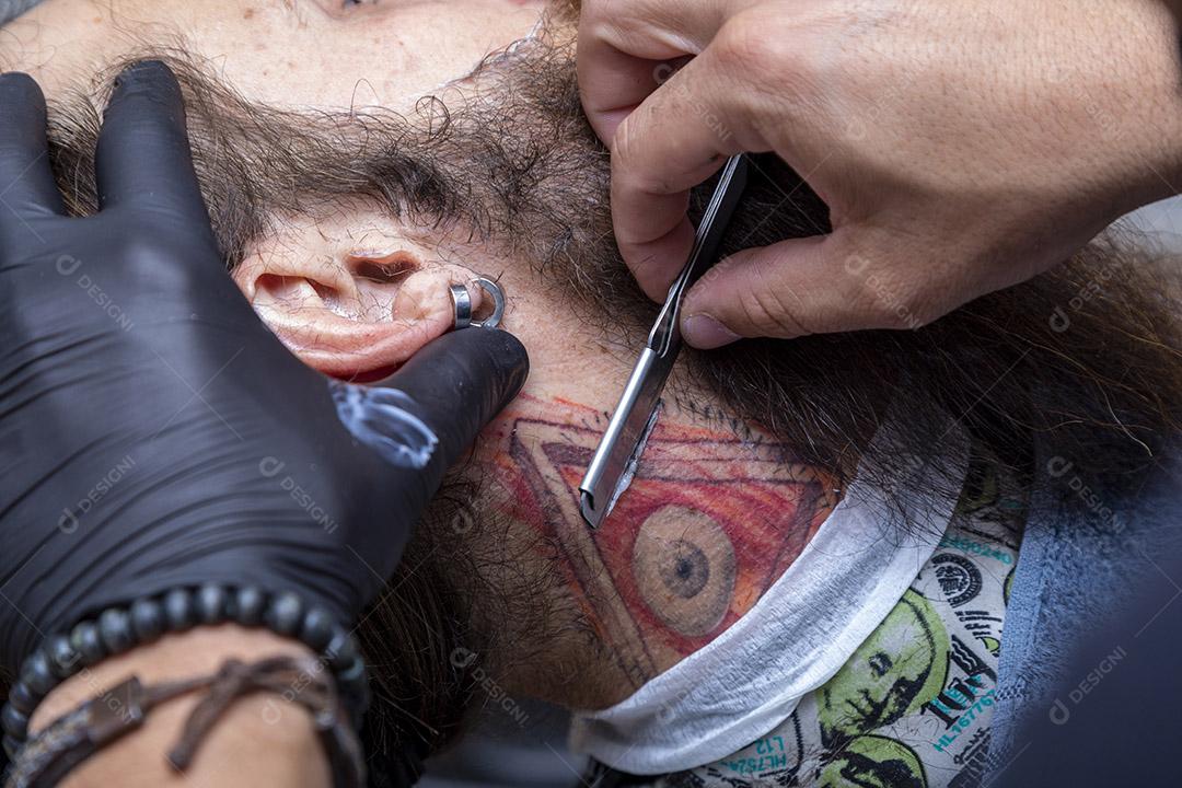 Barbeiro usando barbeador para cortar a barba de um homem. Imagem JPG