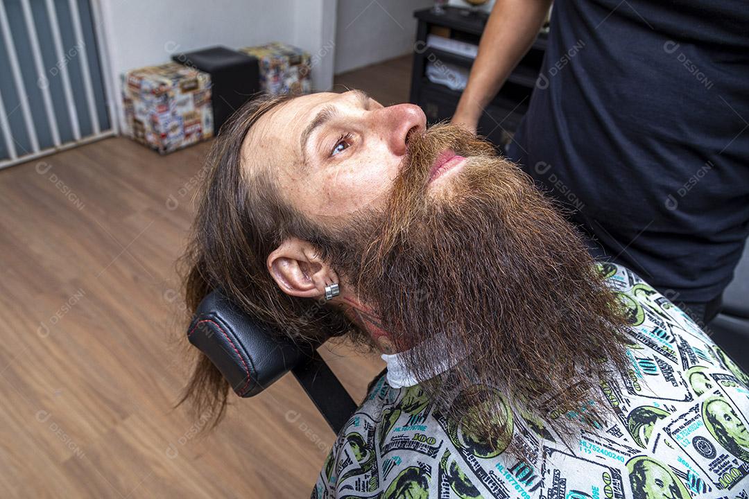 Homem ruivo sentado na cadeira de barbearia exibindo sua bela barba cortada Imagem JPG