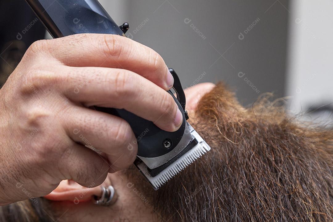 Barbeiro usando barbeador para cortar a barba de um homem. Imagem JPG