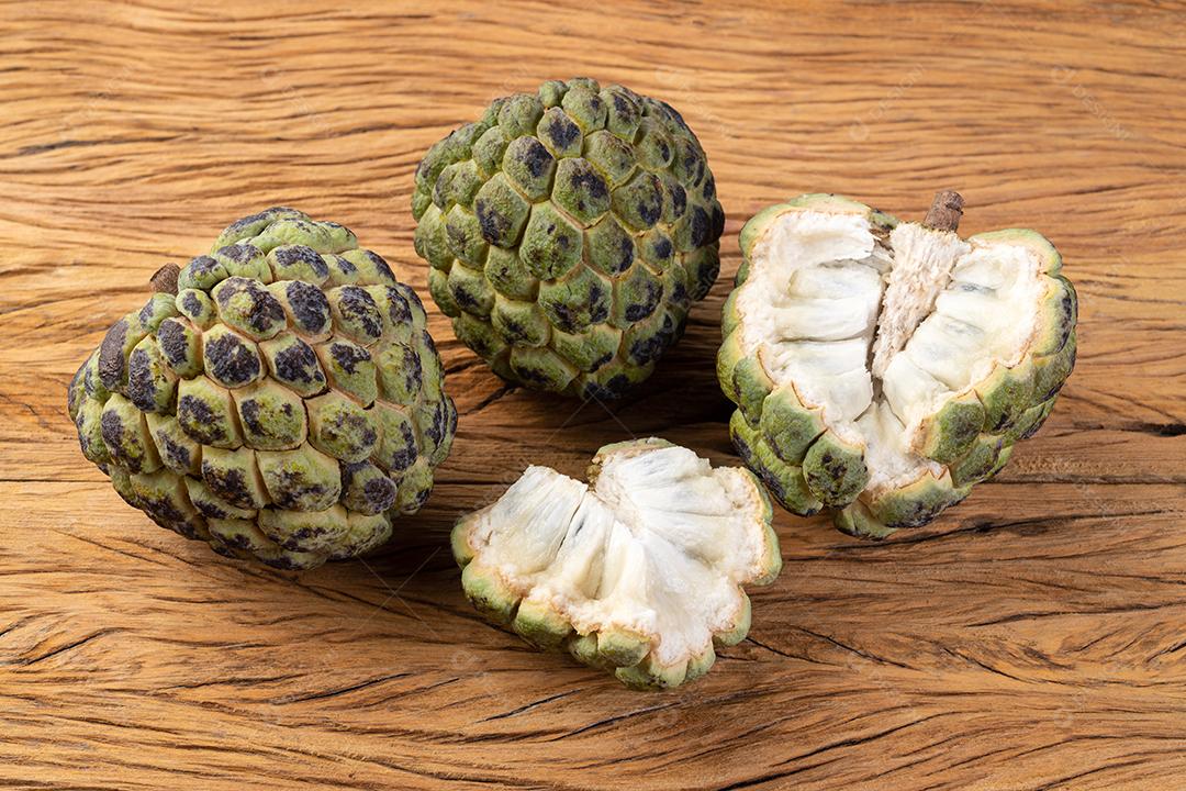 Maçãs de açúcar ou pinha com frutas cortadas sobre a mesa de madeira