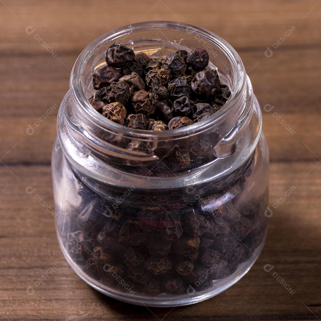 Closeup em frasco de vidro com grãos de pimenta preta em fundo de madeira imagem JPG