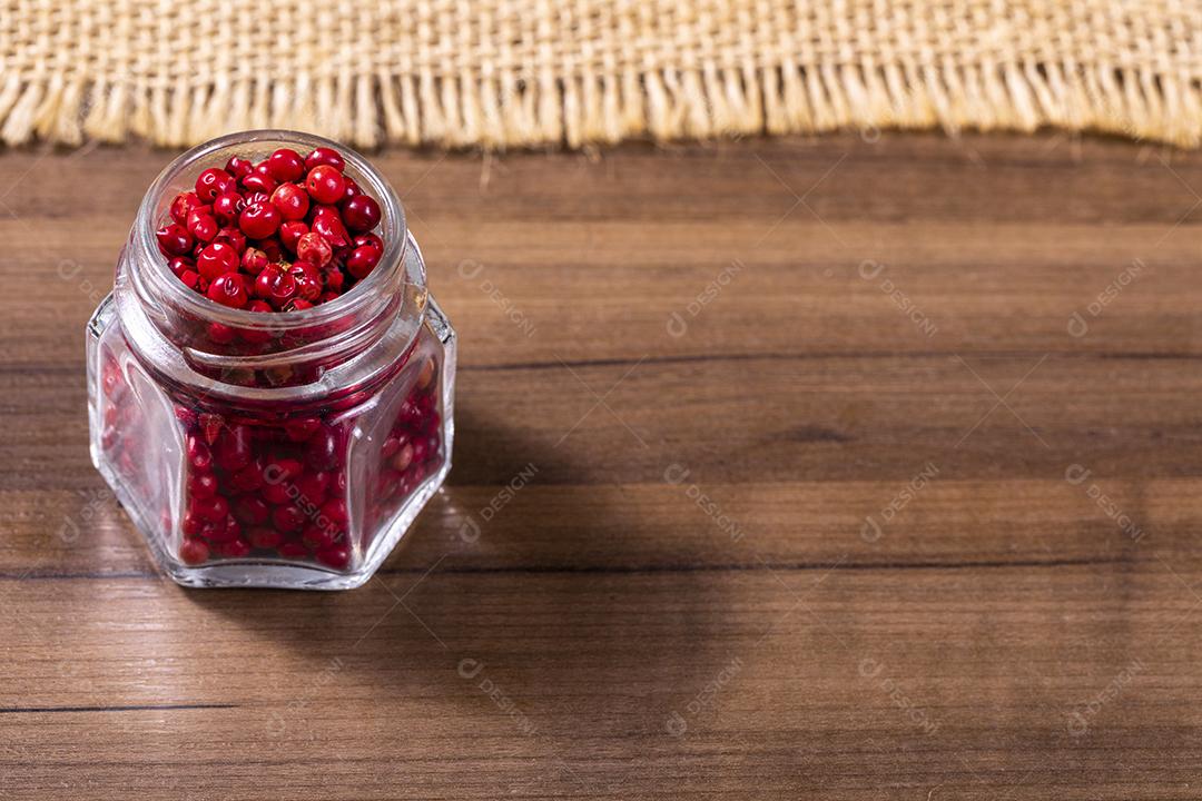 Closeup em frasco de vidro com grãos de pimenta preta em fundo de madeira imagem JPG