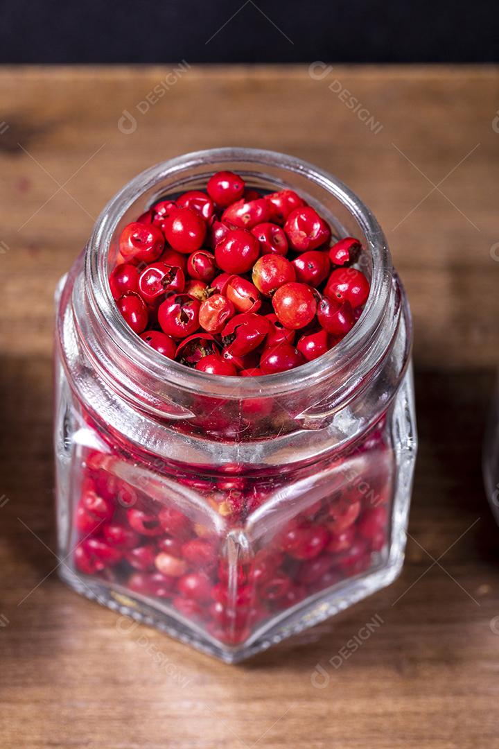 Fotos Closeup em frasco de vidro com grãos de pimenta vermelha em fundo de madeira.