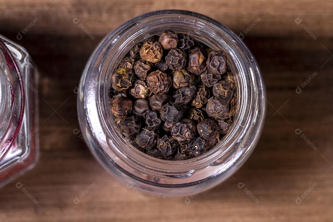 Closeup em frasco de vidro com grãos de pimenta preta em fundo de madeira Imagem JPG